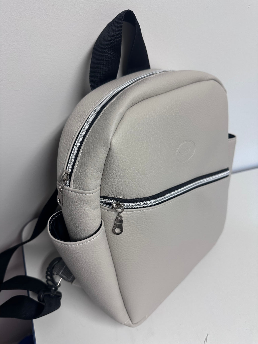 Light grey faux leather backpack with a visible brand logo on a white background