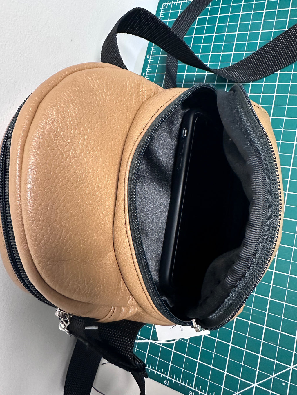 Tan crossbody bag with a phone inside on a white surface