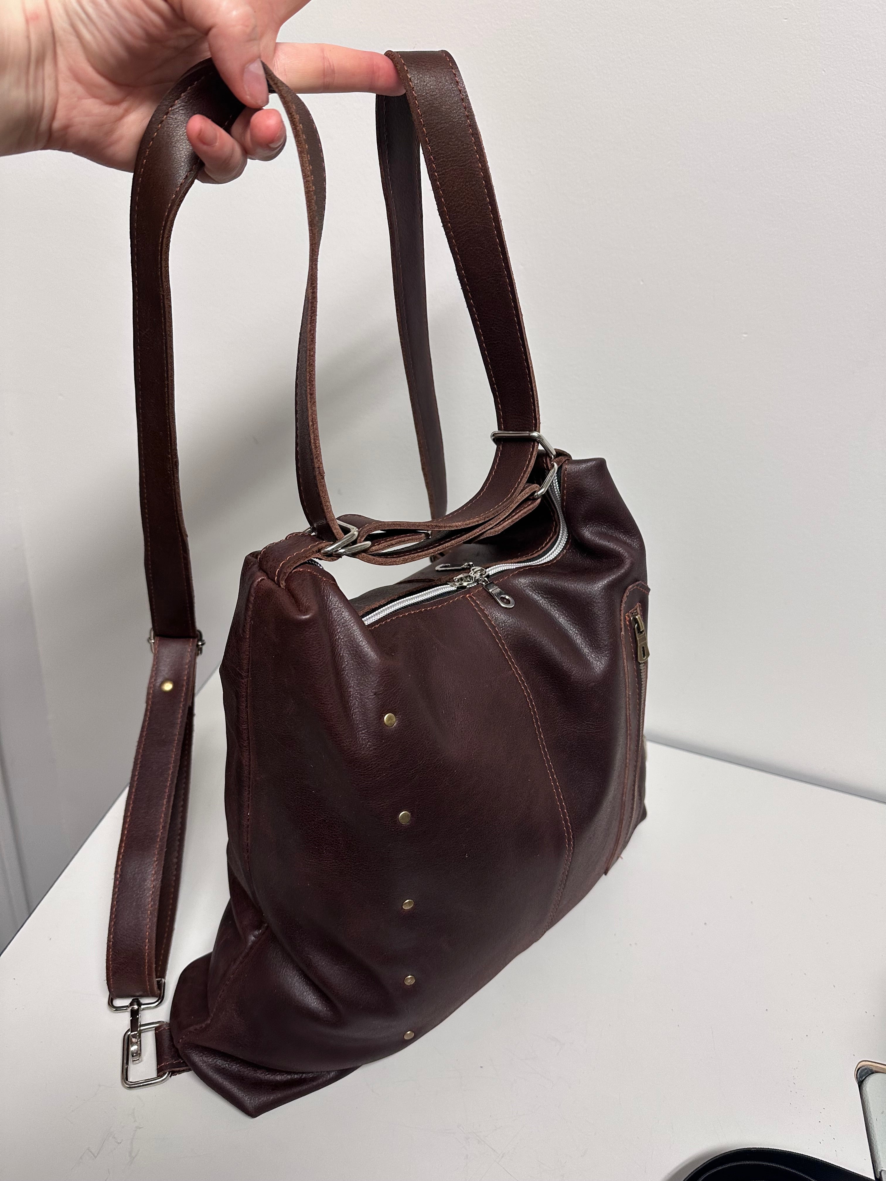 Brown leather bag with a strap held by a hand on a light gray background