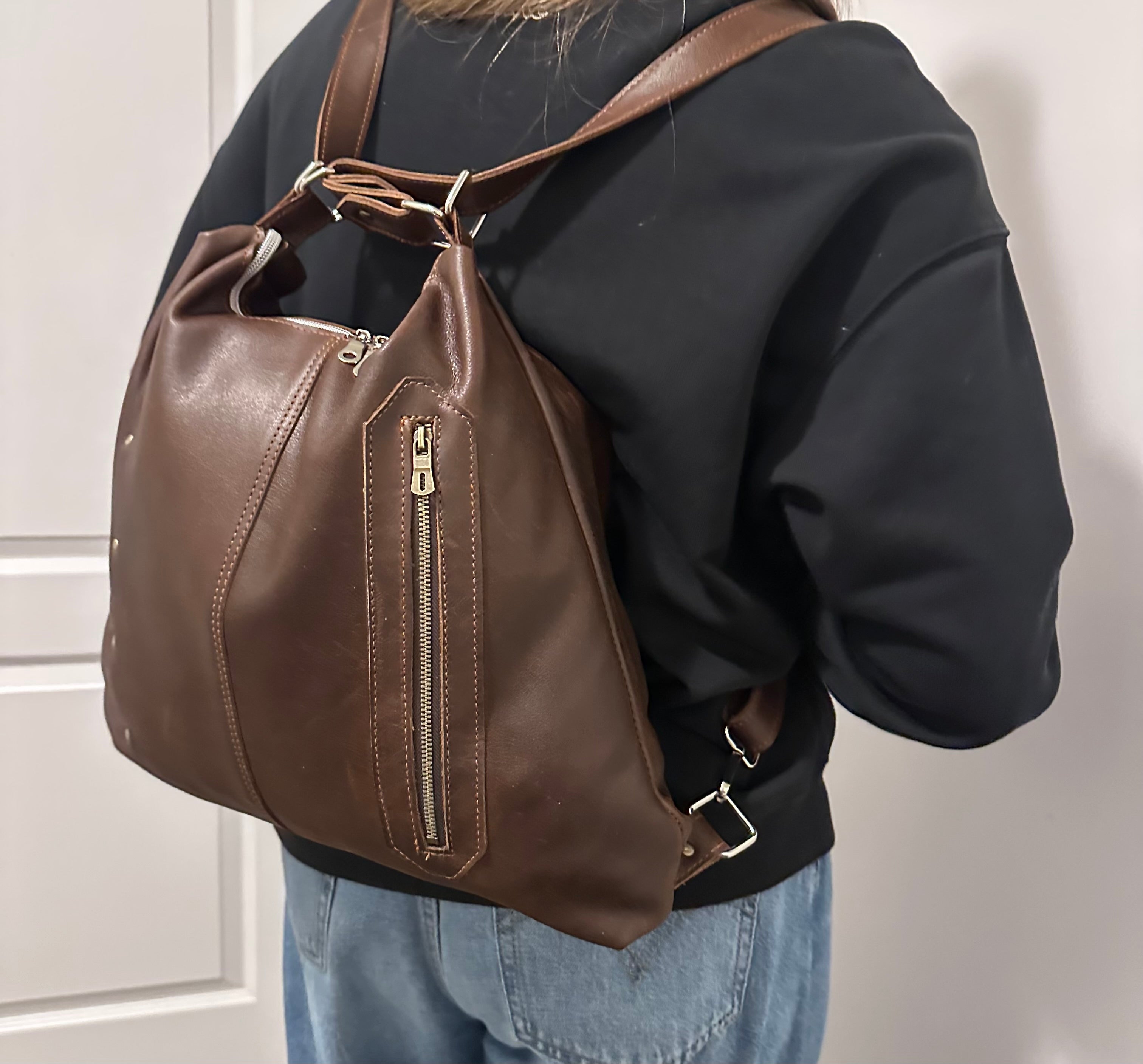 Brown leather backpack worn by a person against a neutral background