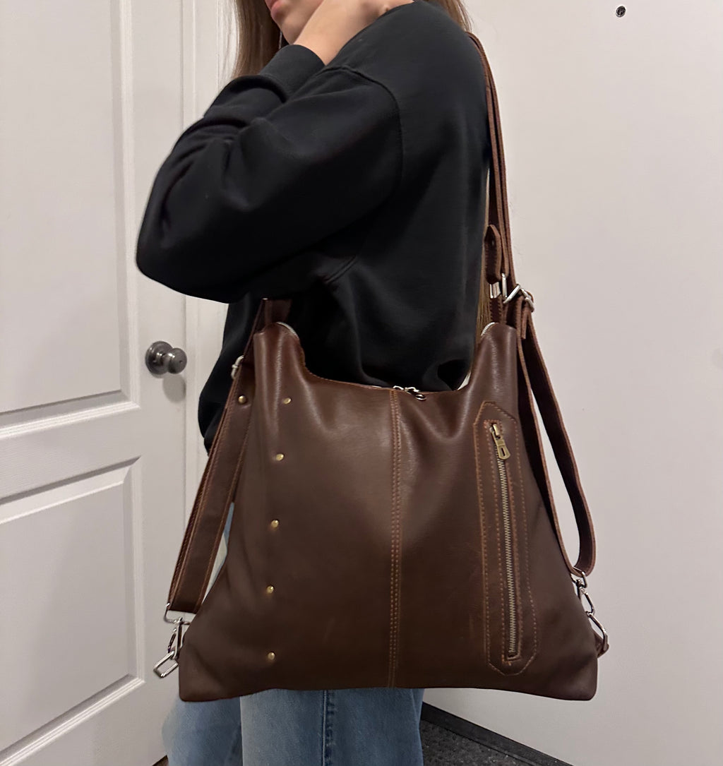 Person holding a brown leather handbag against a neutral background
