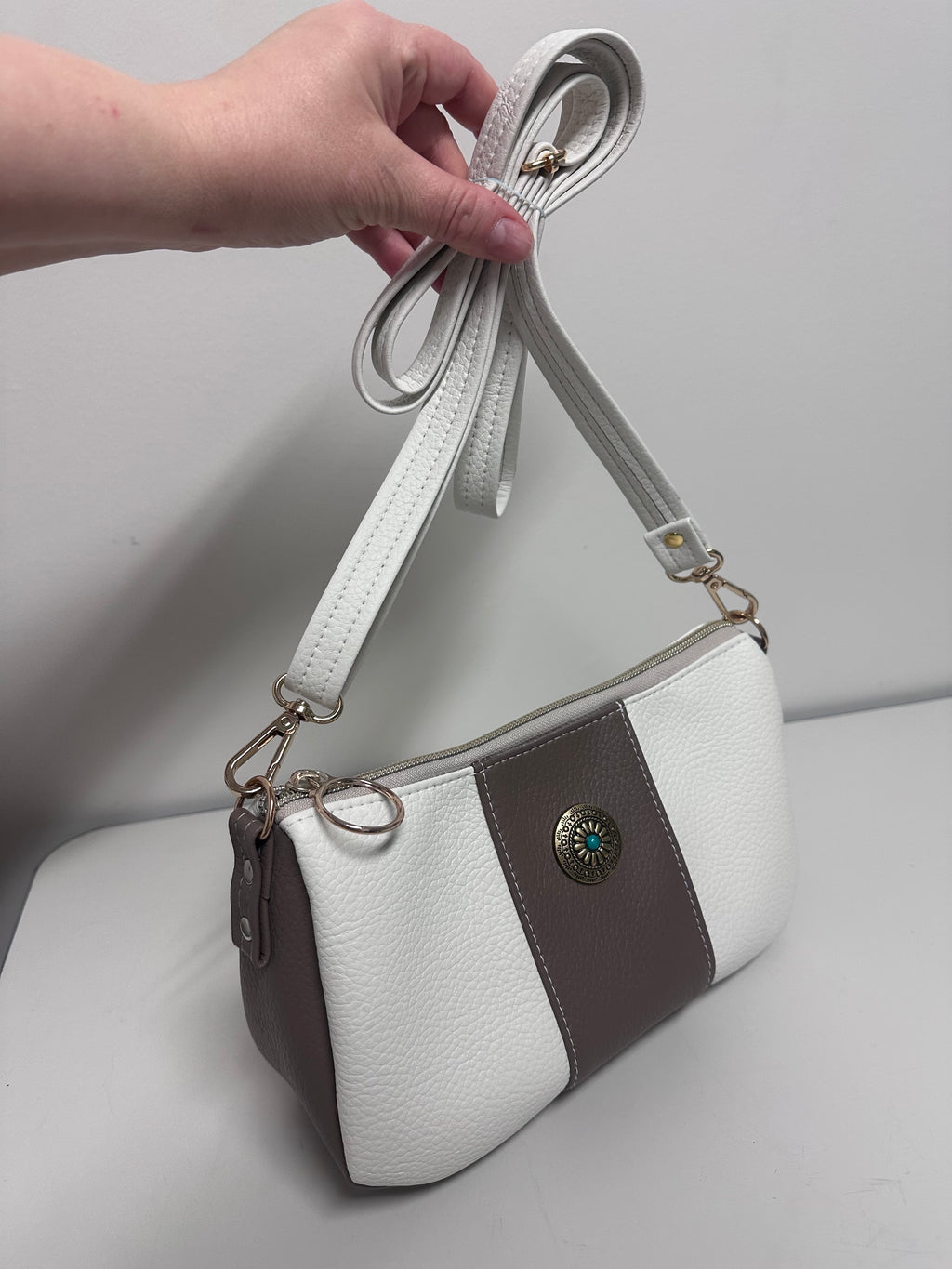 White and tan handbag with a white strap held by a hand against a light gray background