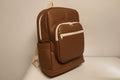Brown faux leather backpack with beige accents on a light gray background