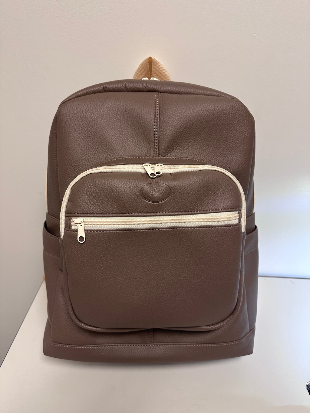 Brown faux leather backpack with a white zipper on a light gray background