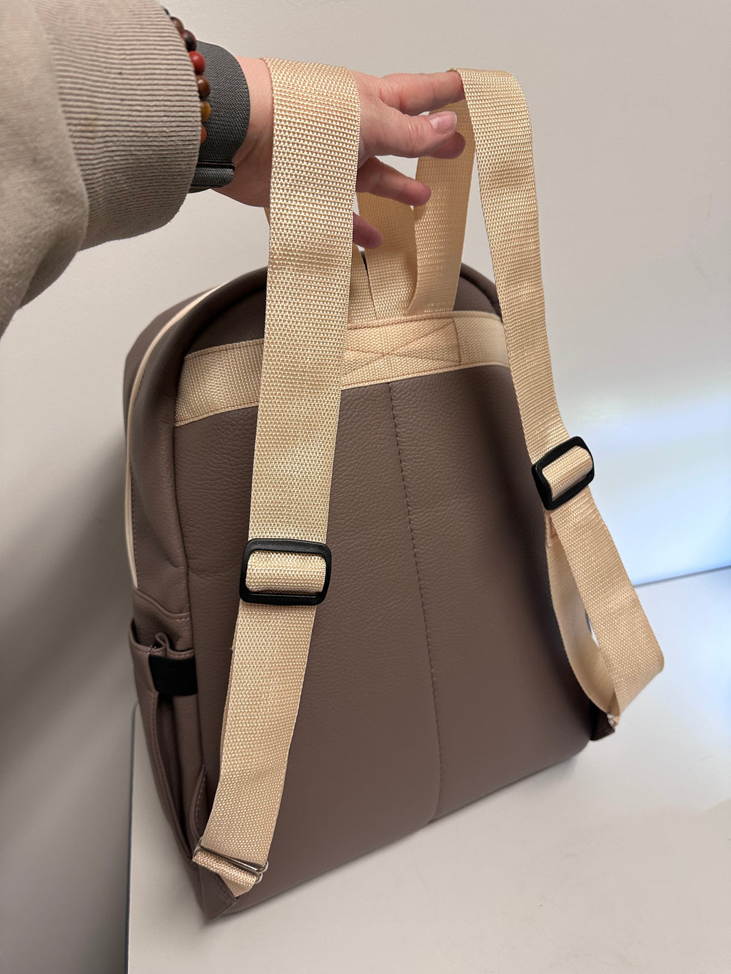 Brown bag with beige strap held by a hand on a light background