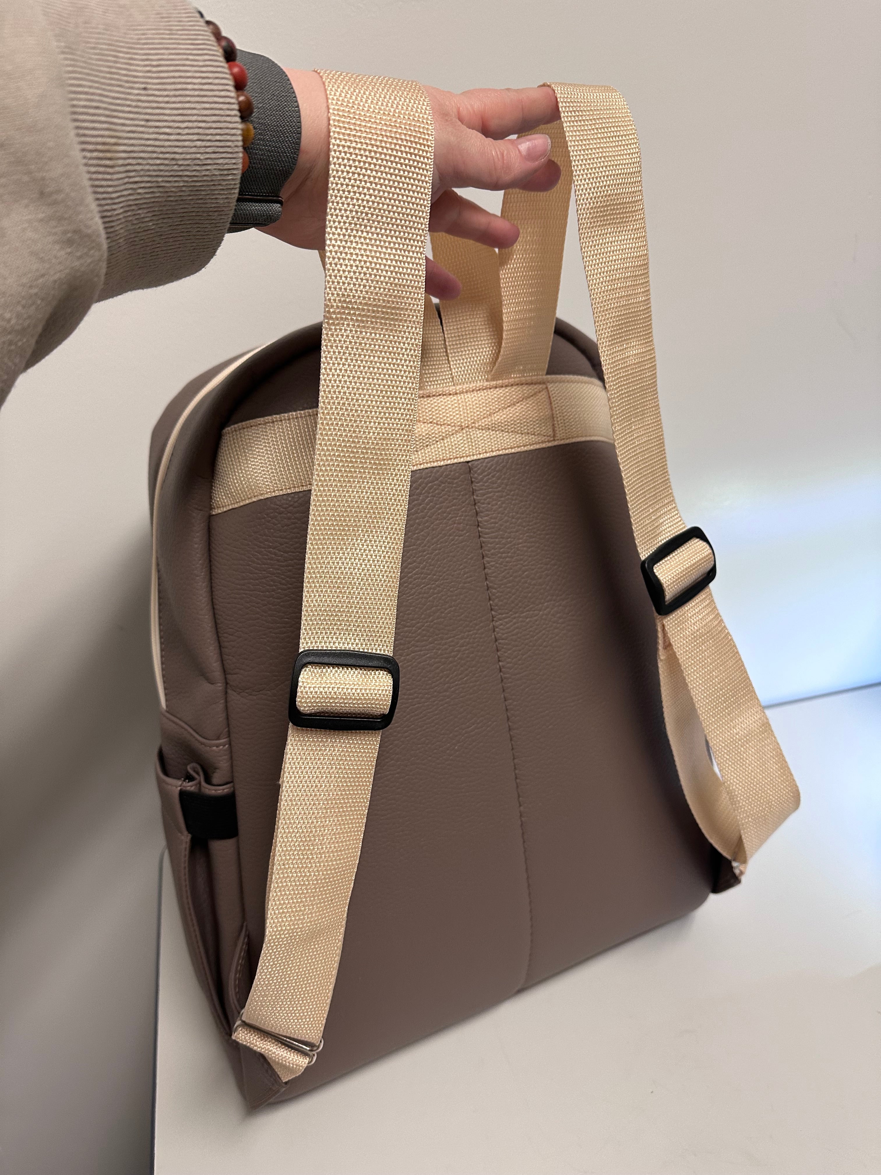 Brown bag with beige strap held by a hand on a light background