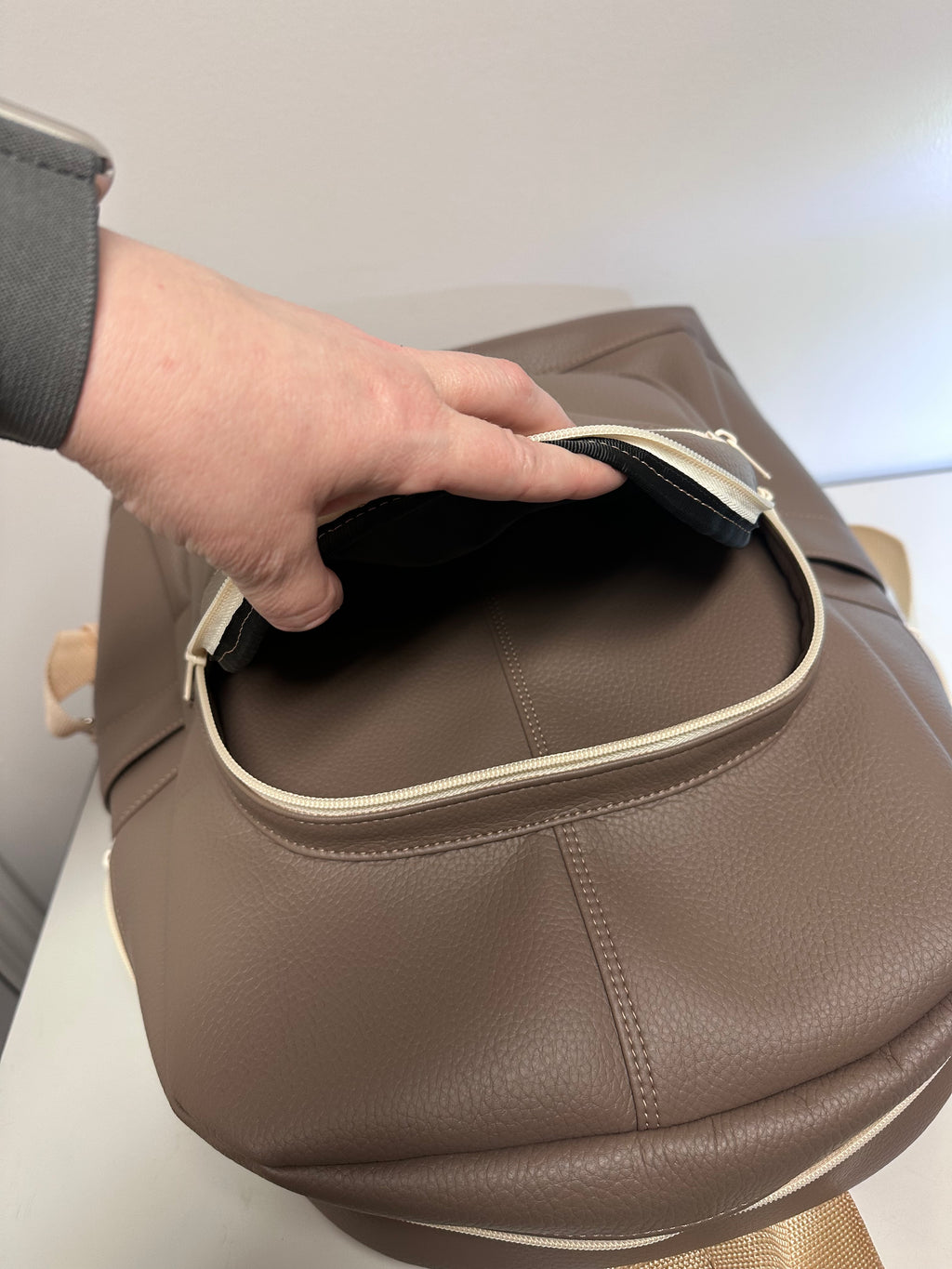 Brown faux leather bag with a hand opening it on a light background