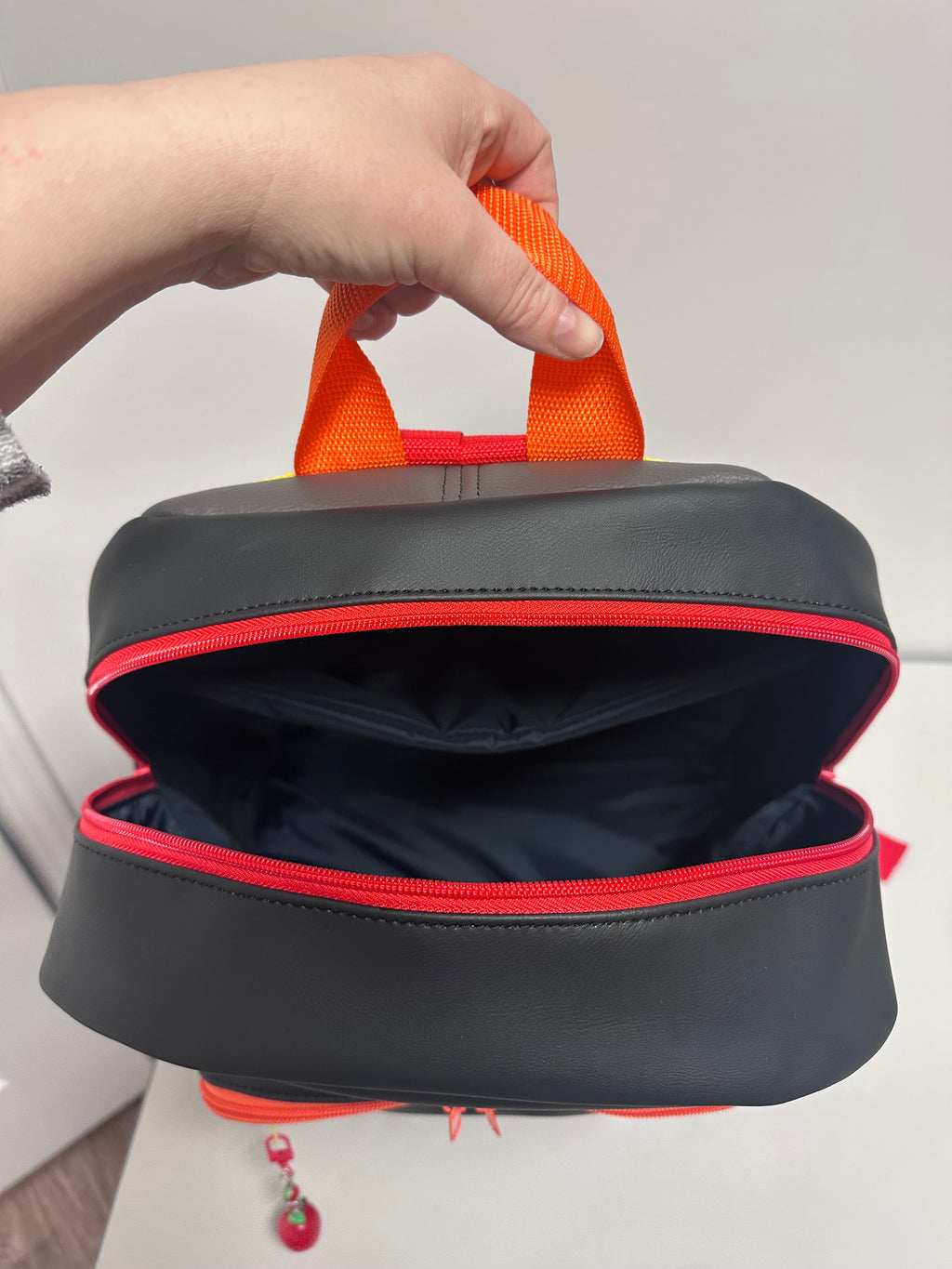 Black bag with orange strap held by a hand against a white background