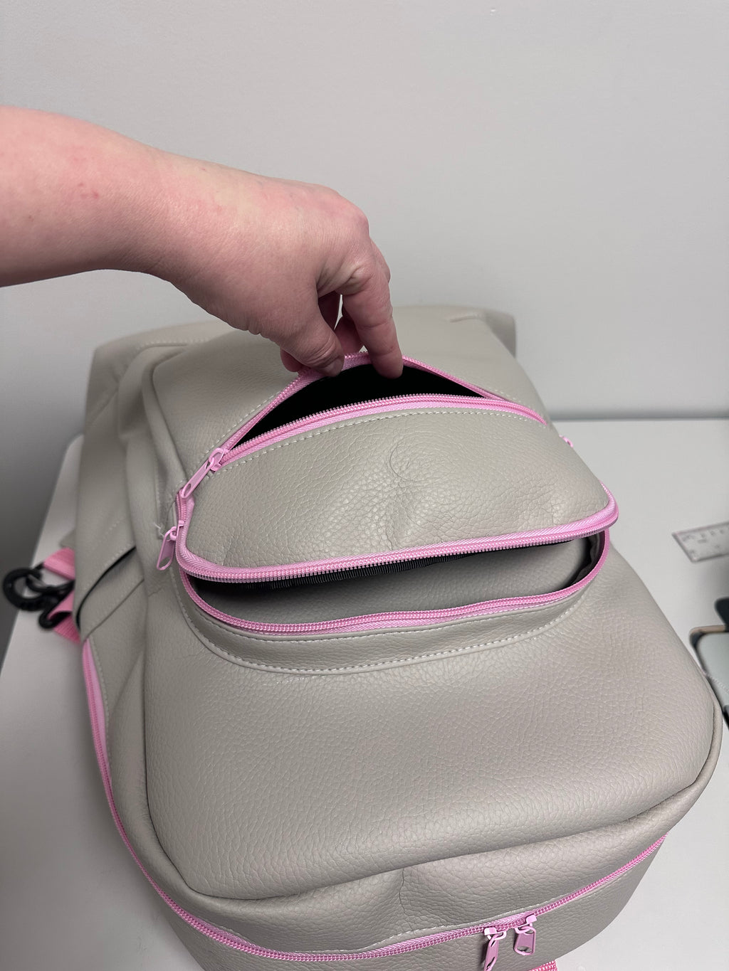 Gray backpack with pink zippers being adjusted by a hand against a white background