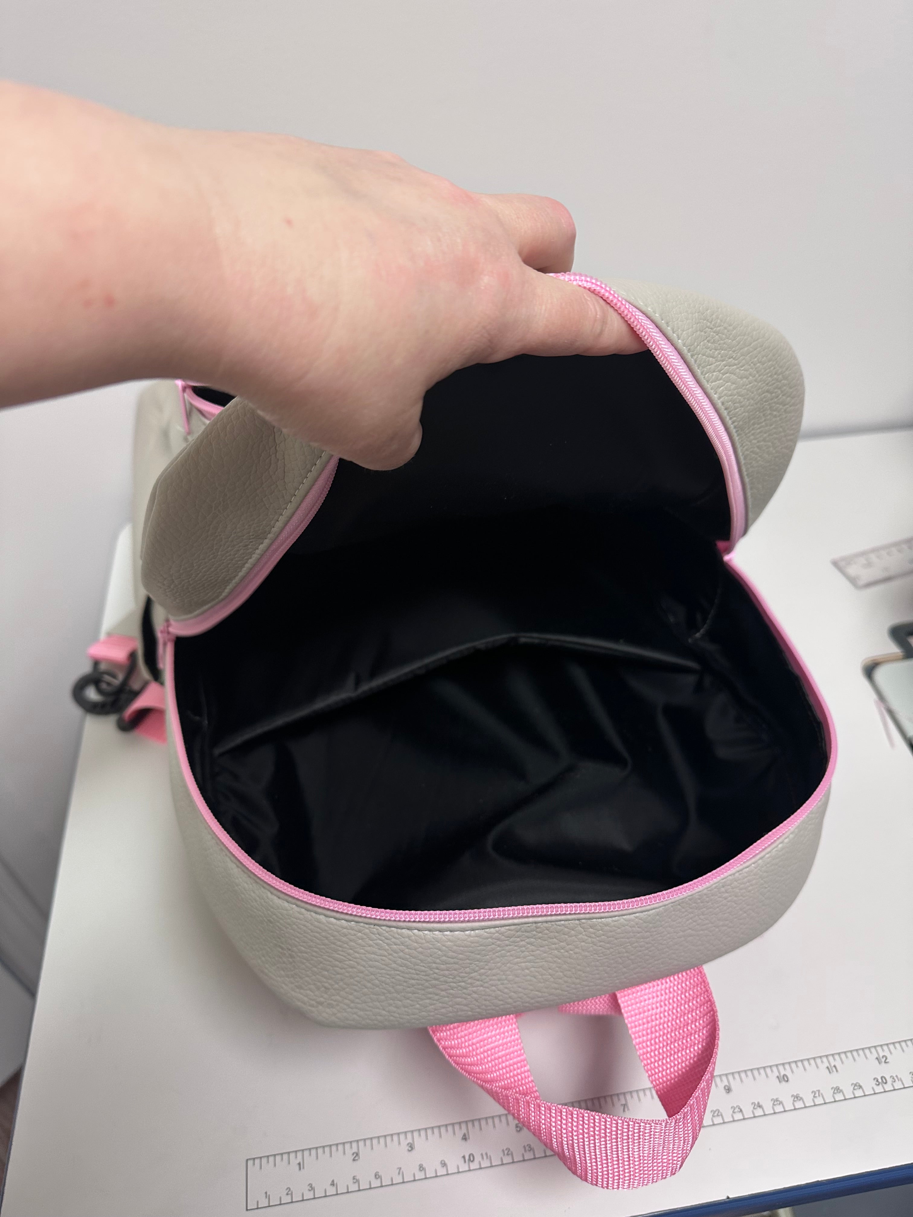 Gray and pink bag with a hand holding it open on a white surface.