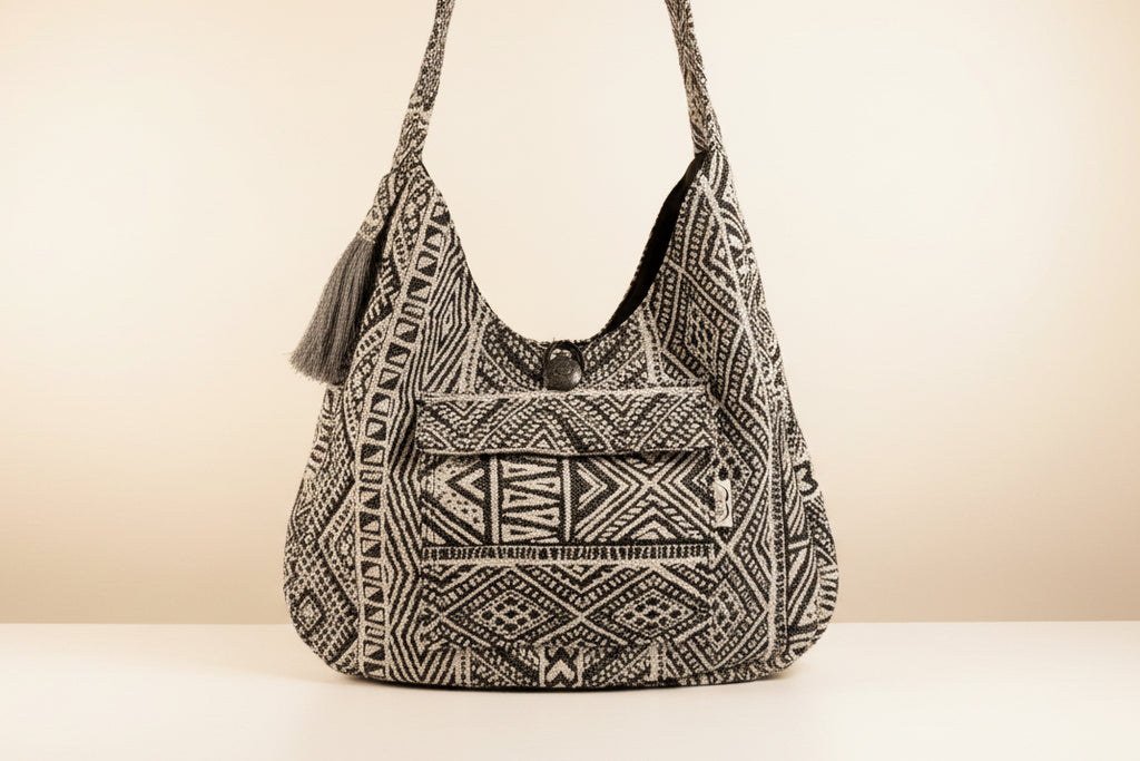Black and white patterned boho crossbody bag with tassel on a beige background