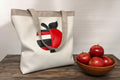 Tote bag with a red and black apple design on a wooden surface