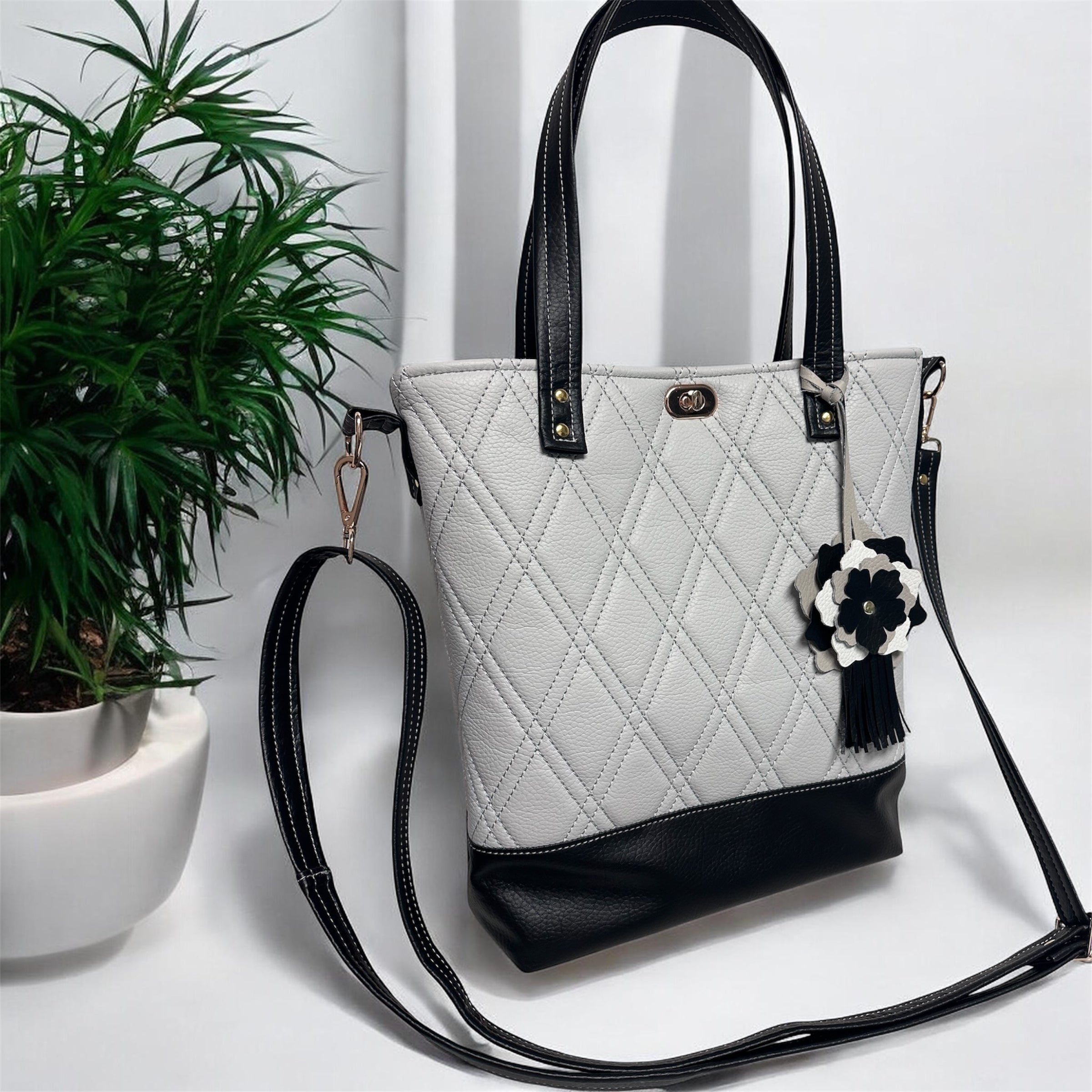 White quilted handbag with black accents on a white surface with a plant in the background